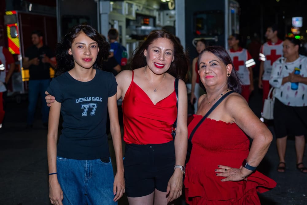 Tres mujeres posando en la verbena, con personal de Cruz Roja al fondo