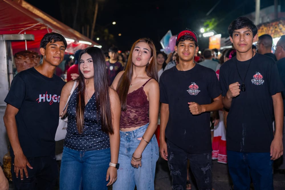 Grupo de cinco jóvenes posando frente al trompo al pastor y los puestos iluminados