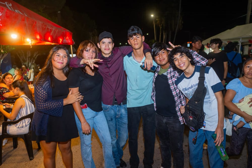 Grupo de seis jóvenes posando bajo las carpas, con las palmeras iluminadas al fondo