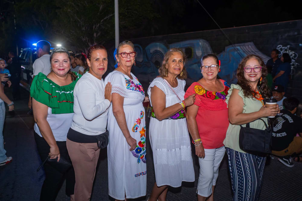 Grupo de mujeres con blusas bordadas y listones tricolores posando en la calle