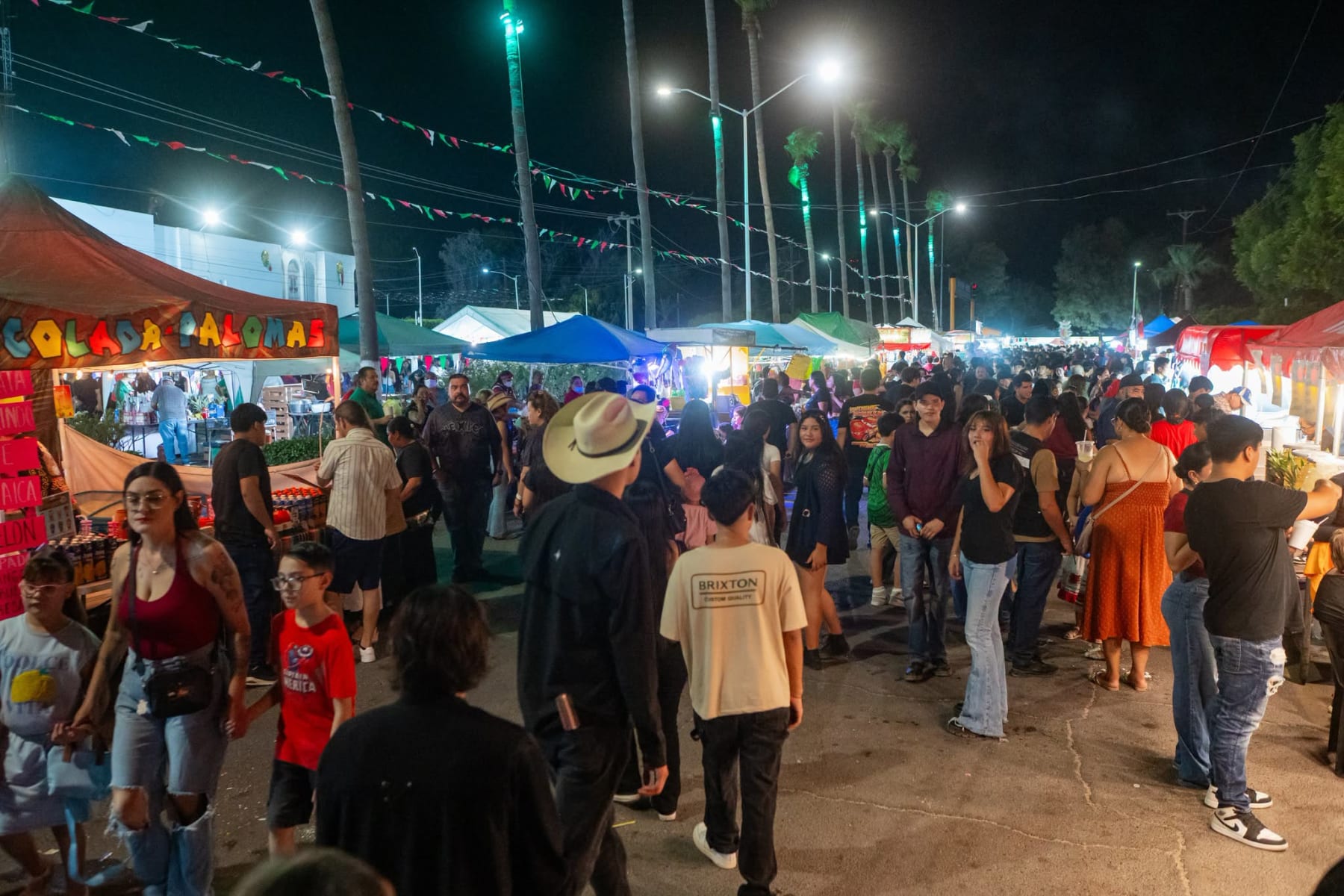 Calle del centro de Puerto Peñasco con palmeras iluminadas de verde, banderines tricolores y multitud durante la noche del Grito