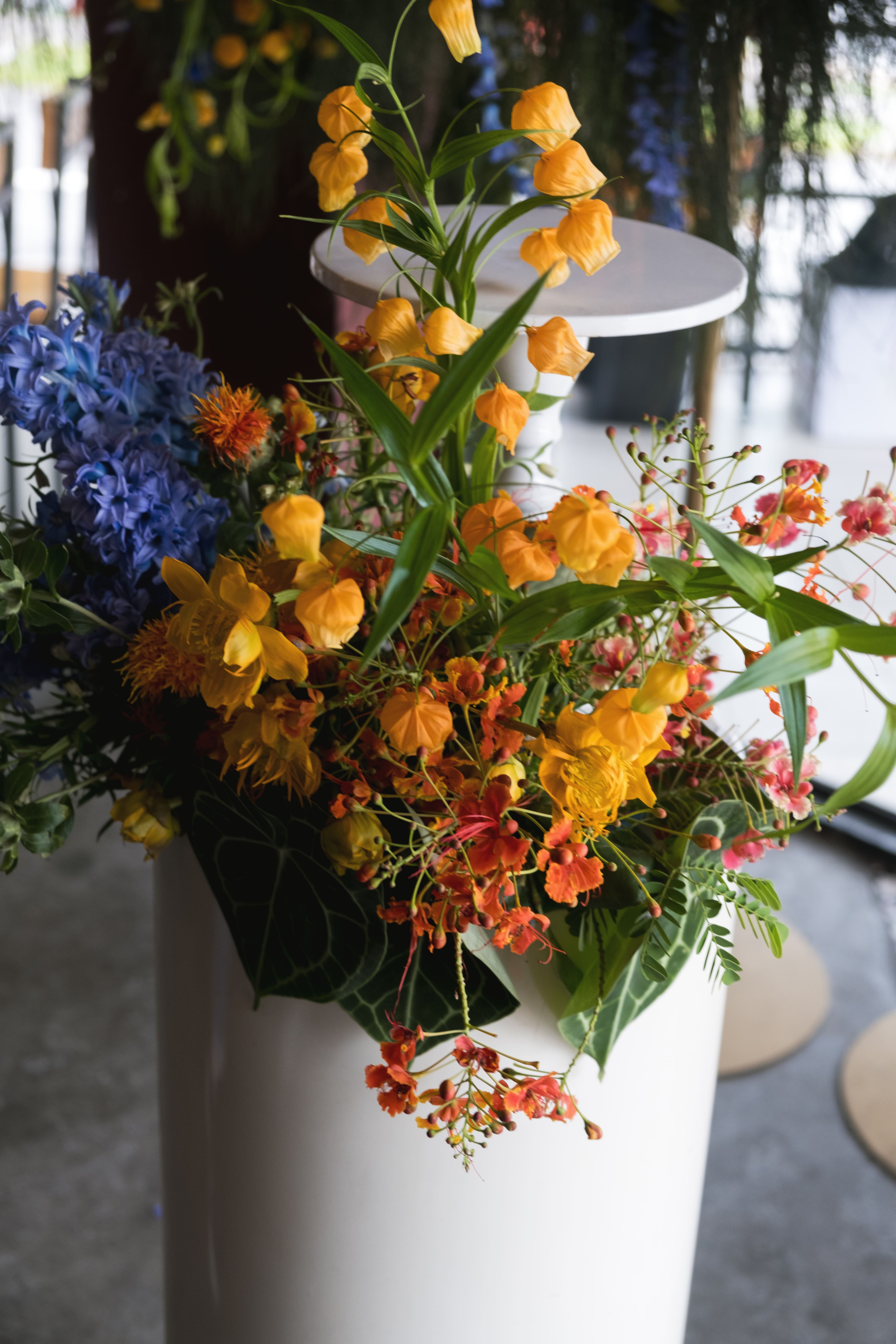 Floral arrangement with orange, blue and yellow tones on top a pedestal.