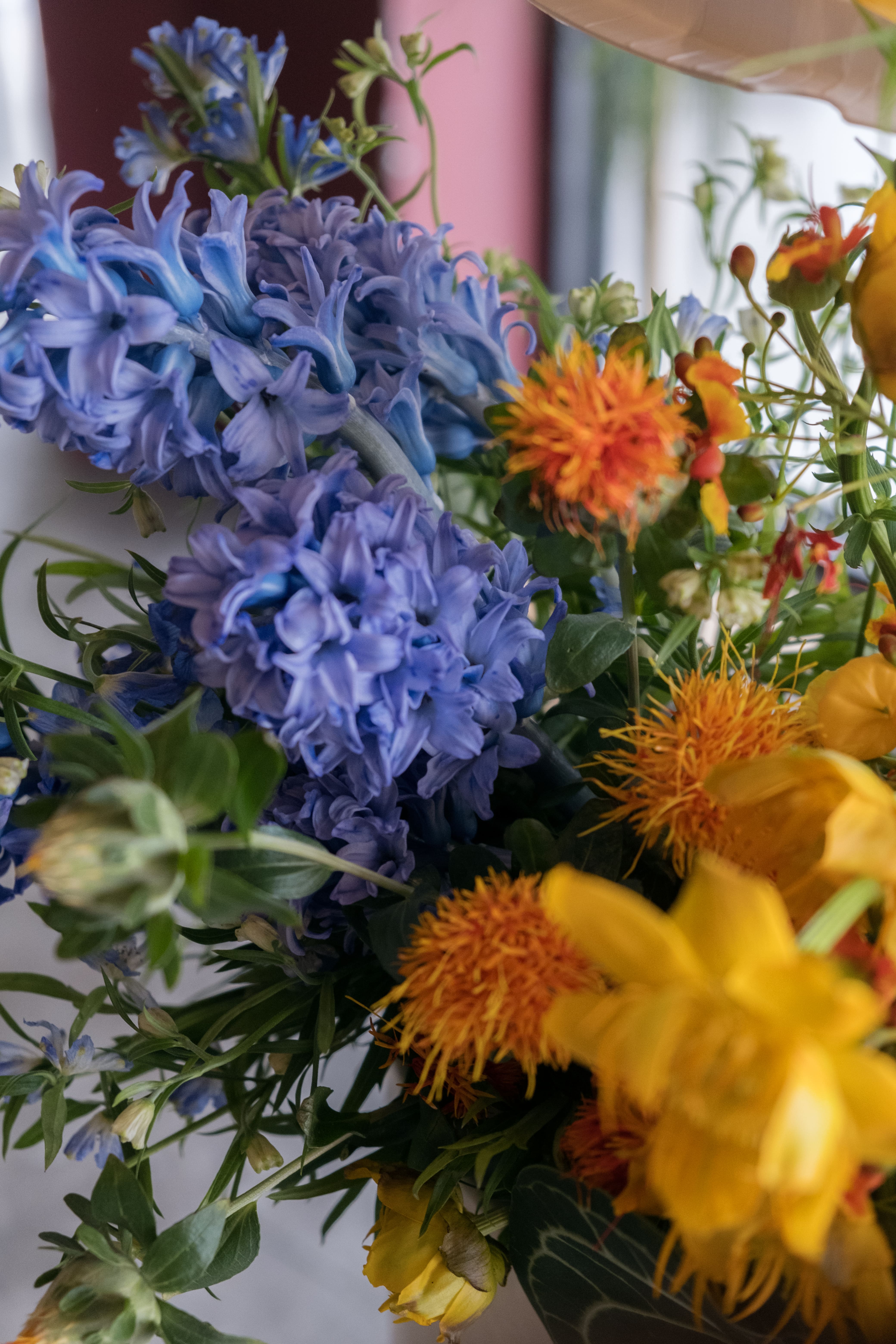 Bold hues floral arrangement on a pedestal featuring blue delphinium, peacock flowers and chinese latern lilies. 