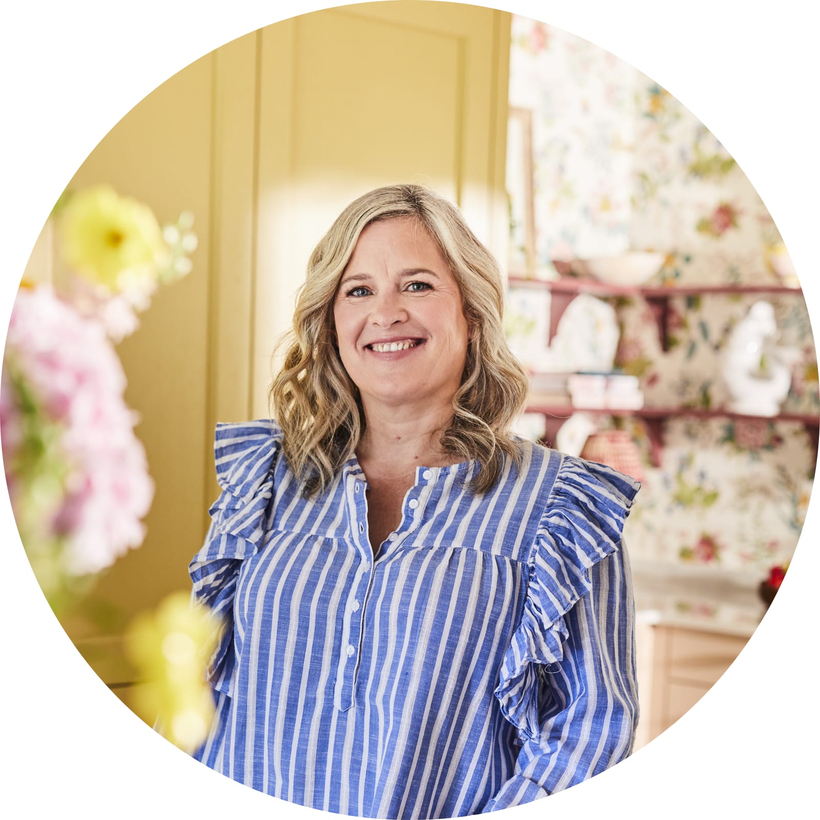 Sophie wearing a striped blouse, posing by the kitchen island in her colourful kitchen with Magnet colours harvest and Clalk blush in the background