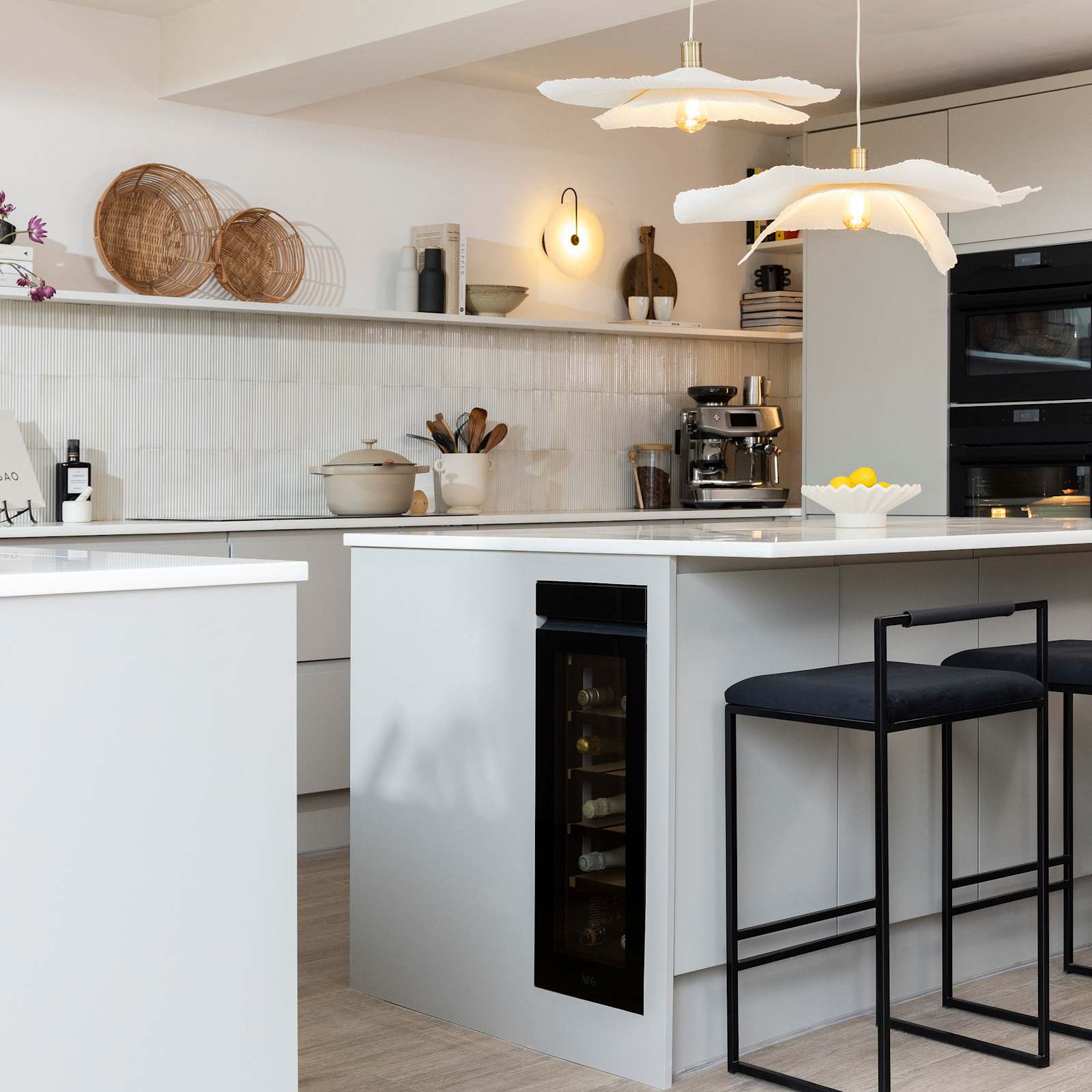 Diagnonal view of kitchen island corner in Yasmin Wyatt's open, light and airy neutral shade handleless Luna kitchen from Magnet with a white Corian worktop in Onyx, two AEG ovens integrated into tall cabinet and a wine cooler integrated into kitchen island.