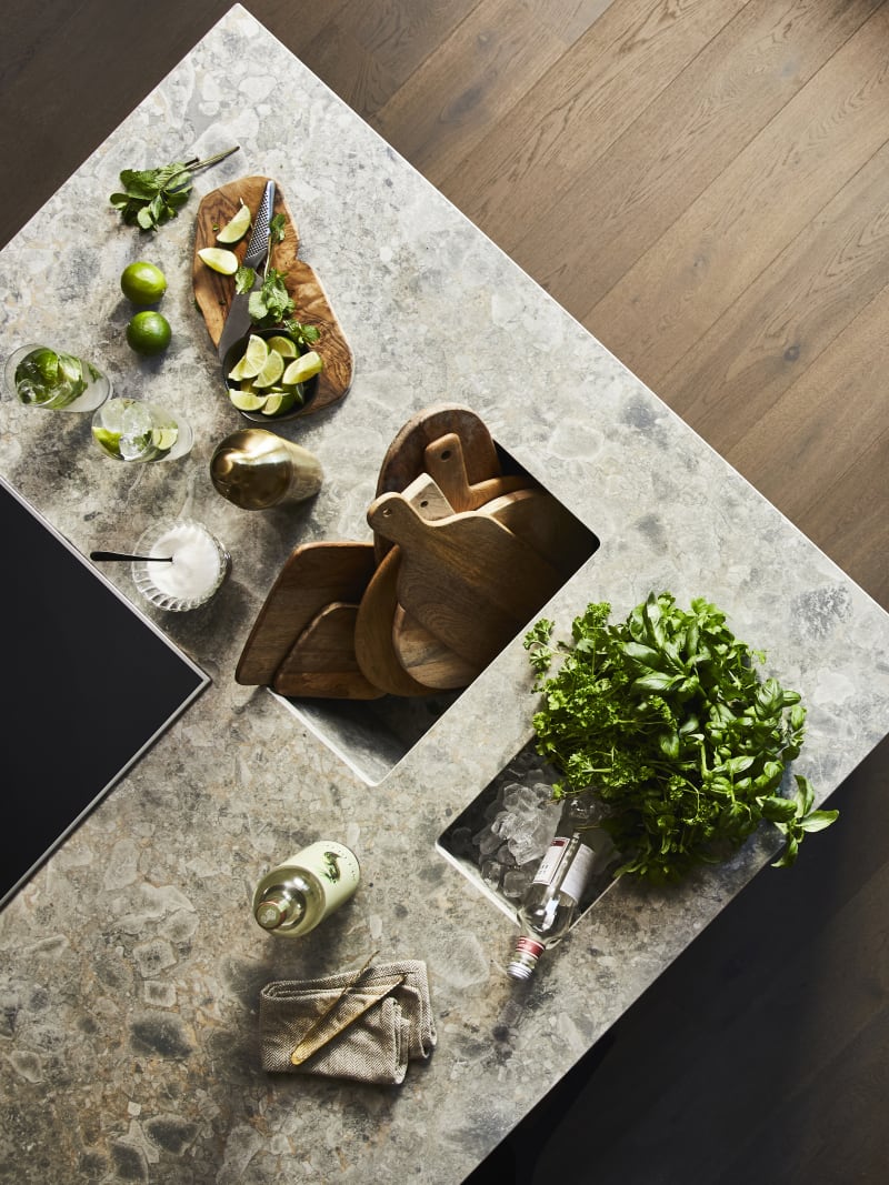 Birds eye view of kitchen island with Dekton in Ceppo worktop,wooden cutting boards with cut up lime fruits and a large plant of basil.