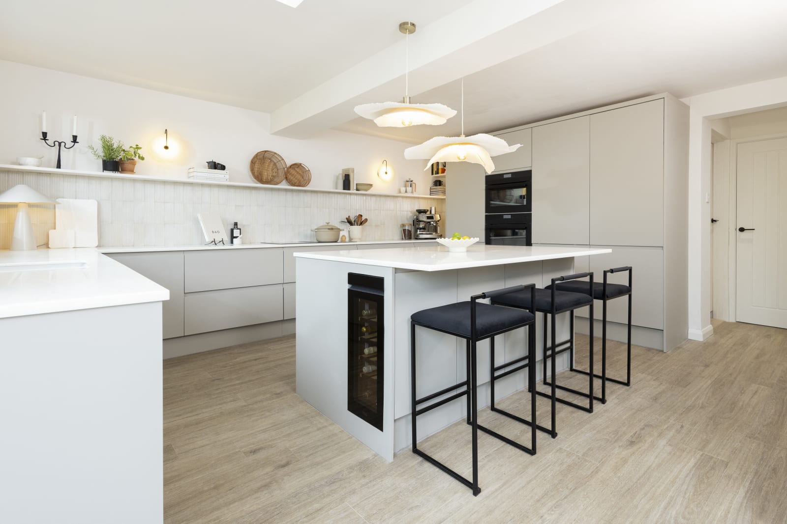 Yasmin Wyatt's kitchen island in the neutral shade Luna kitchen from Magnet with a white Corian worktop, integrated whitegoods and black metal chairs by the kitchen island bar area.