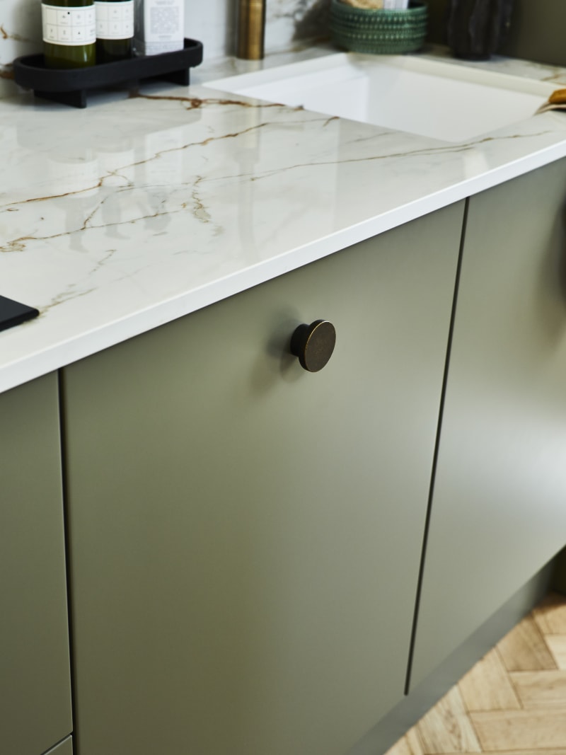 Close-up of Soho green Balmoral cabinet and black handles, with light gray marble worktop and white sink.