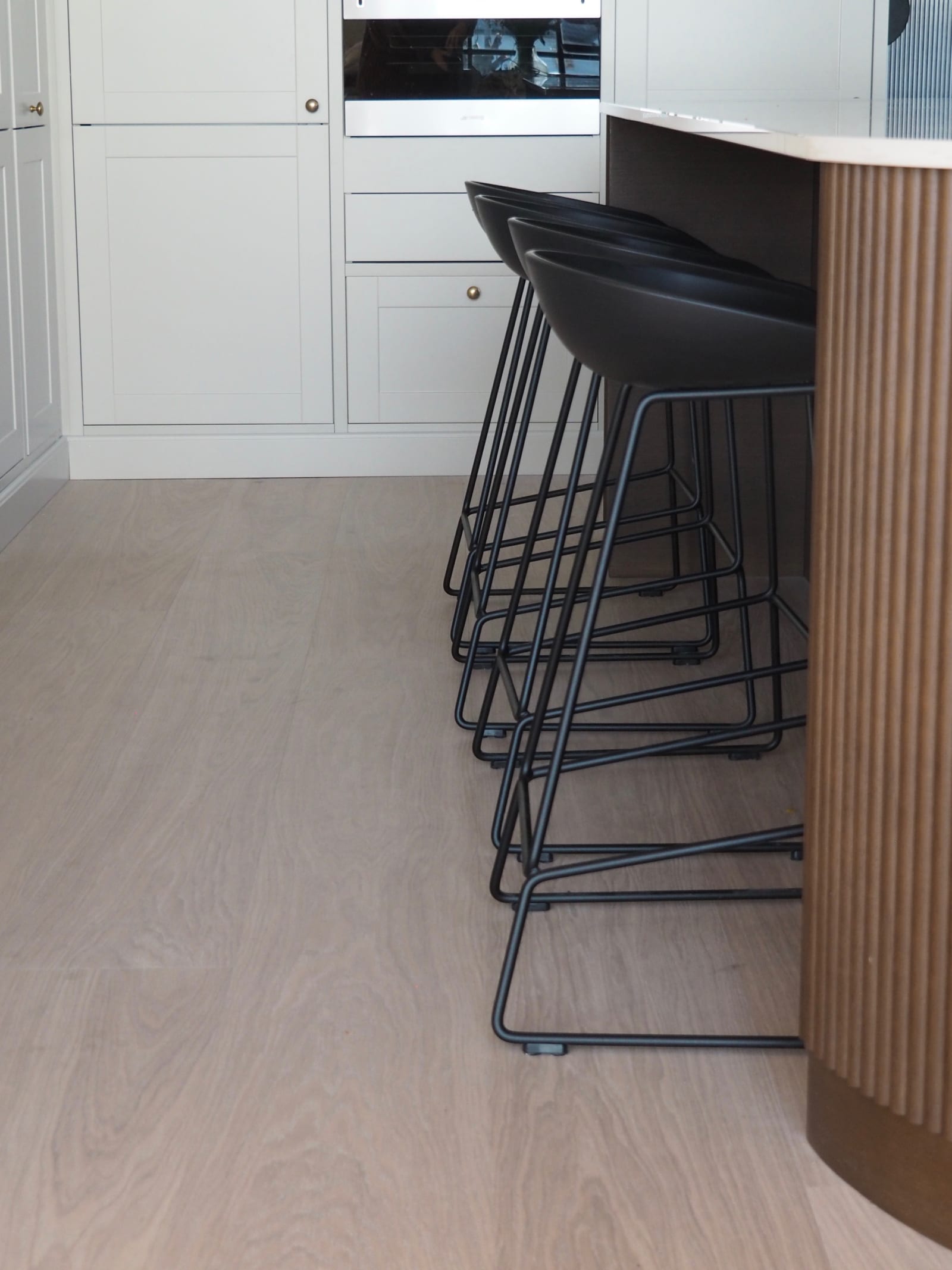 Enden af ​​den afrundede køkkenø med mørkt træpanel, Dekton Taga bordplade og sorte barstole