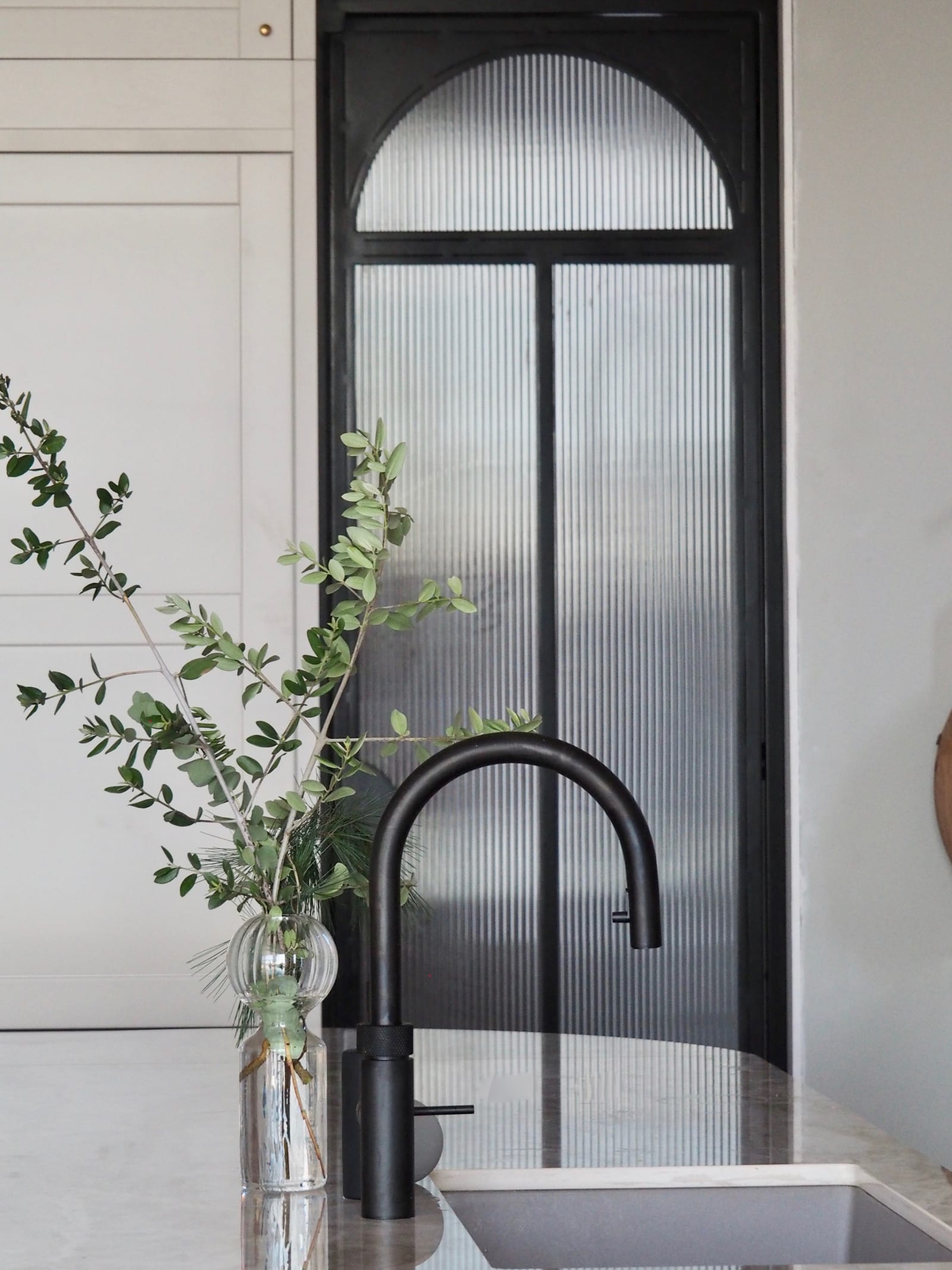 Nærbillede af sort Quooker vandhane i køkkenet med Dekton Taga bordplade og en vase med grønne kviste