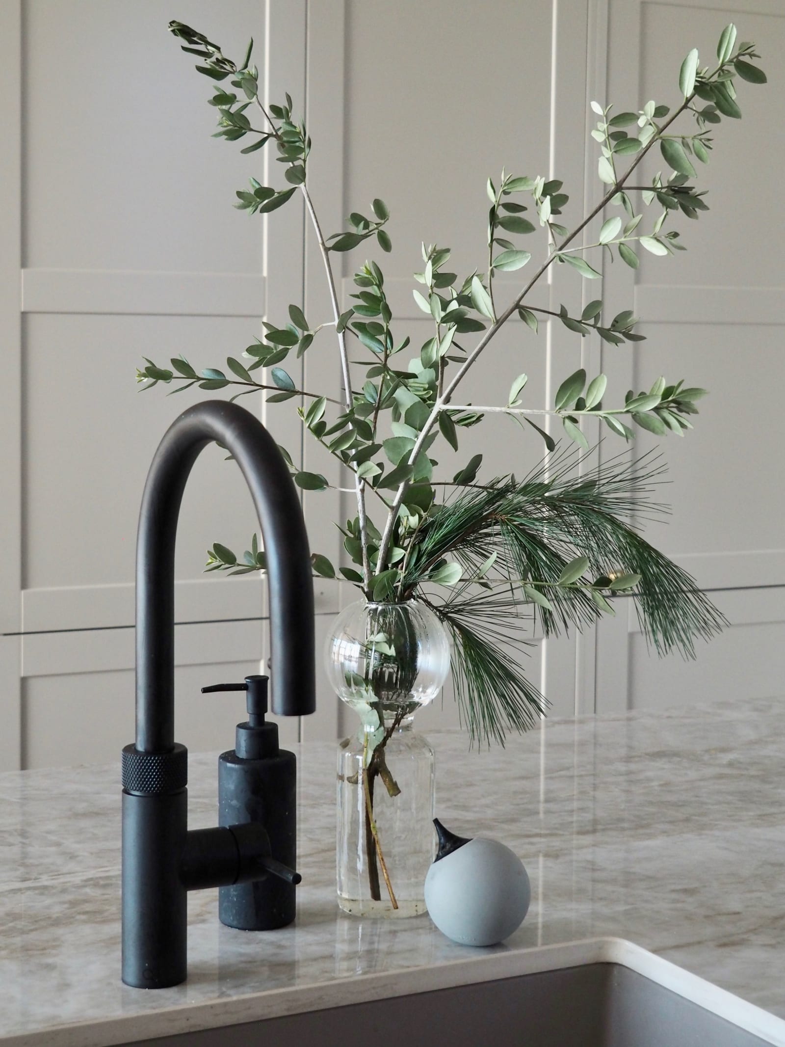 Nærbillede af sort Quooker vandhane i køkkenet med Dekton Taga bordplade og en vase med grønne kviste