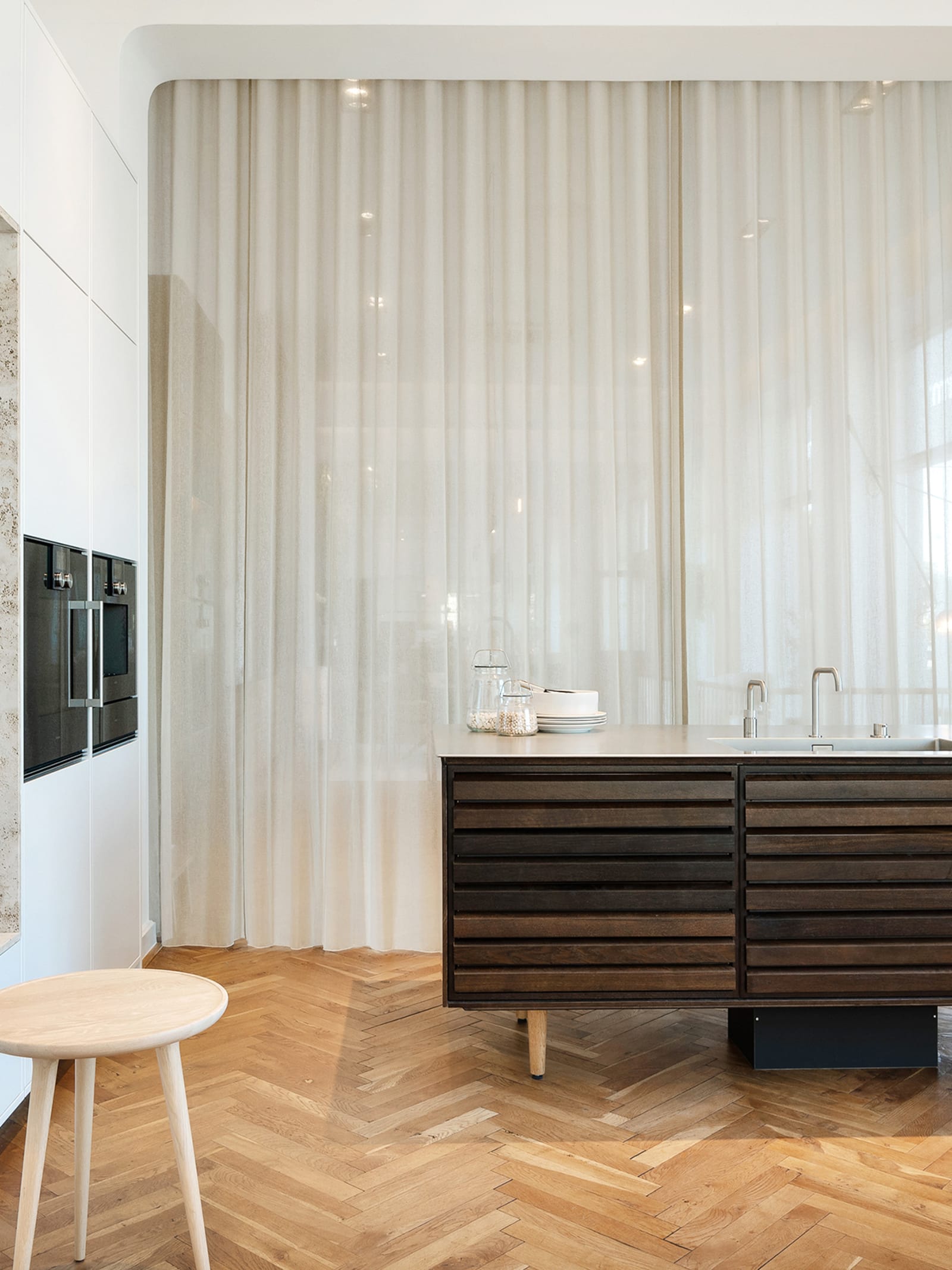 Lounge atmosphere with a kitchen island in smoked oak, white tall cabinets and herringbone floor in oak