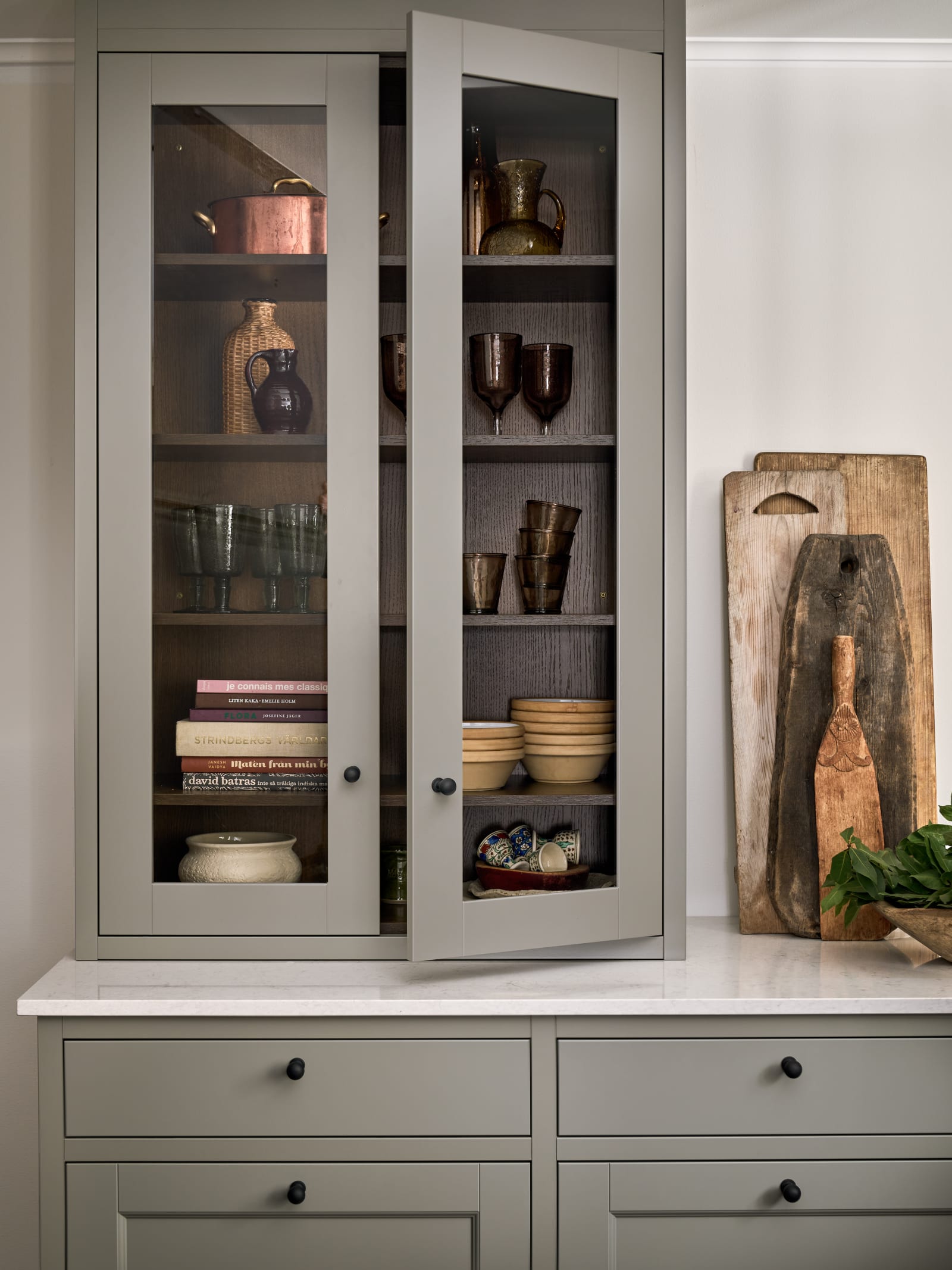 Vitrinskåp ovanpå köksbänken, med matchande greige-målad träram runt glaset och svarta knoppar, i det lantliga köket Fagerö Frö från Marbodal hemma hos Malin Berghagen.