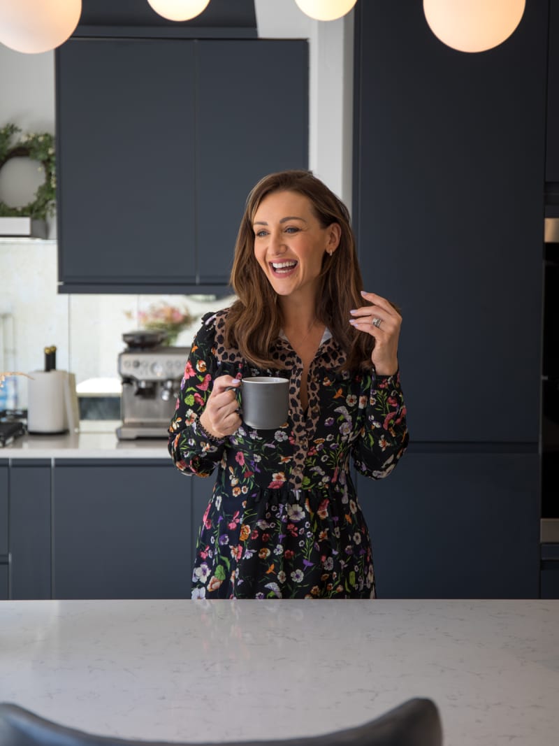 Cath Tyldesley laughing and holding a cup in her chic and contemporary handleless Luna Midnight kitchen from Magnet.