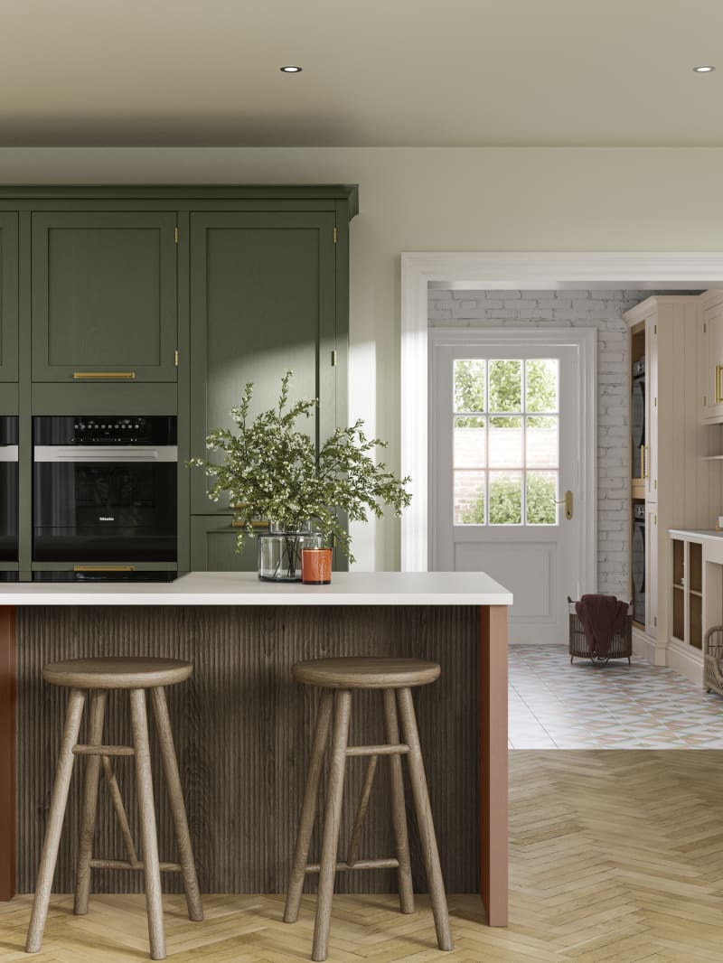 Tall Wardley kitchen cabinets  with built-in ovens, a kitchen island in shade Clay with wooden panelling by seating area and matching wooden bar stools.