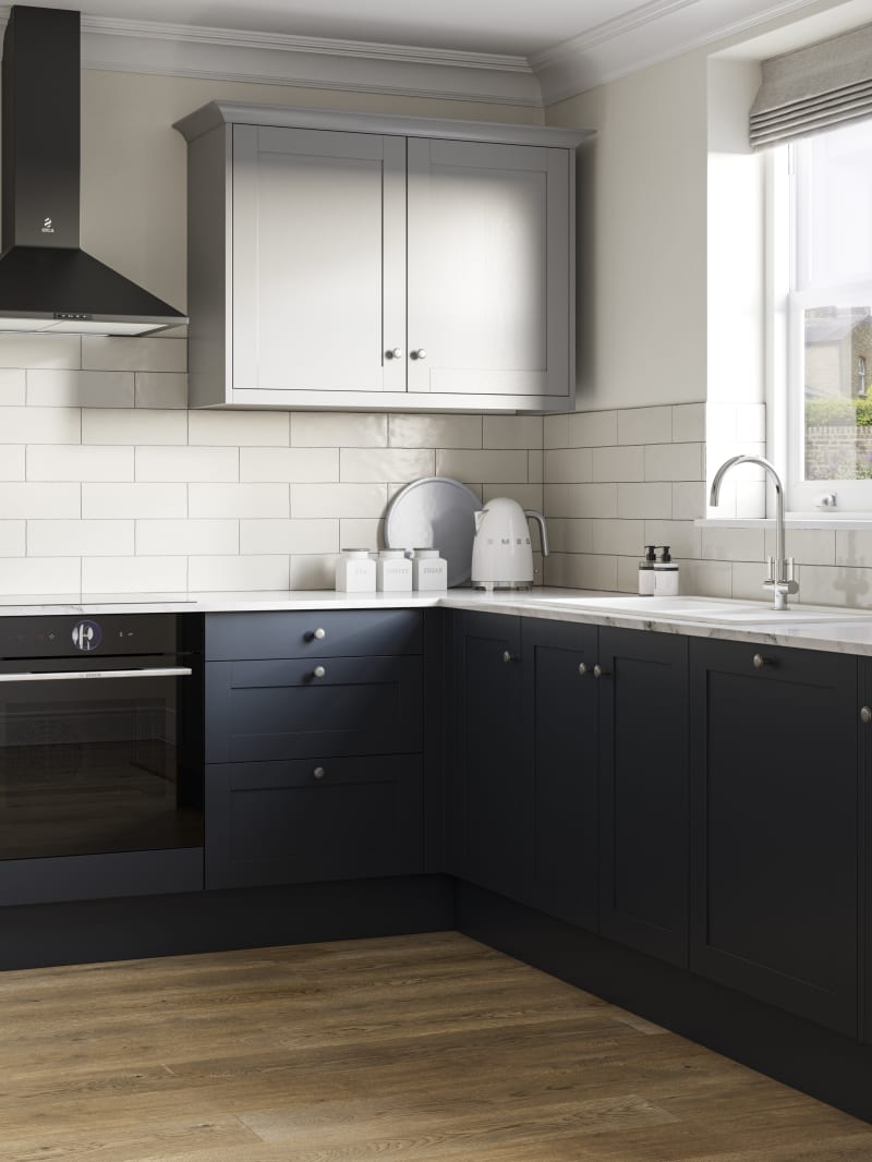 Tatton kitchen from Magnet with cabinetry in dark blue shade Midnight paired with light grey wall cabinets over countertops, white worktop, and white sink by a window, light wooden floors.