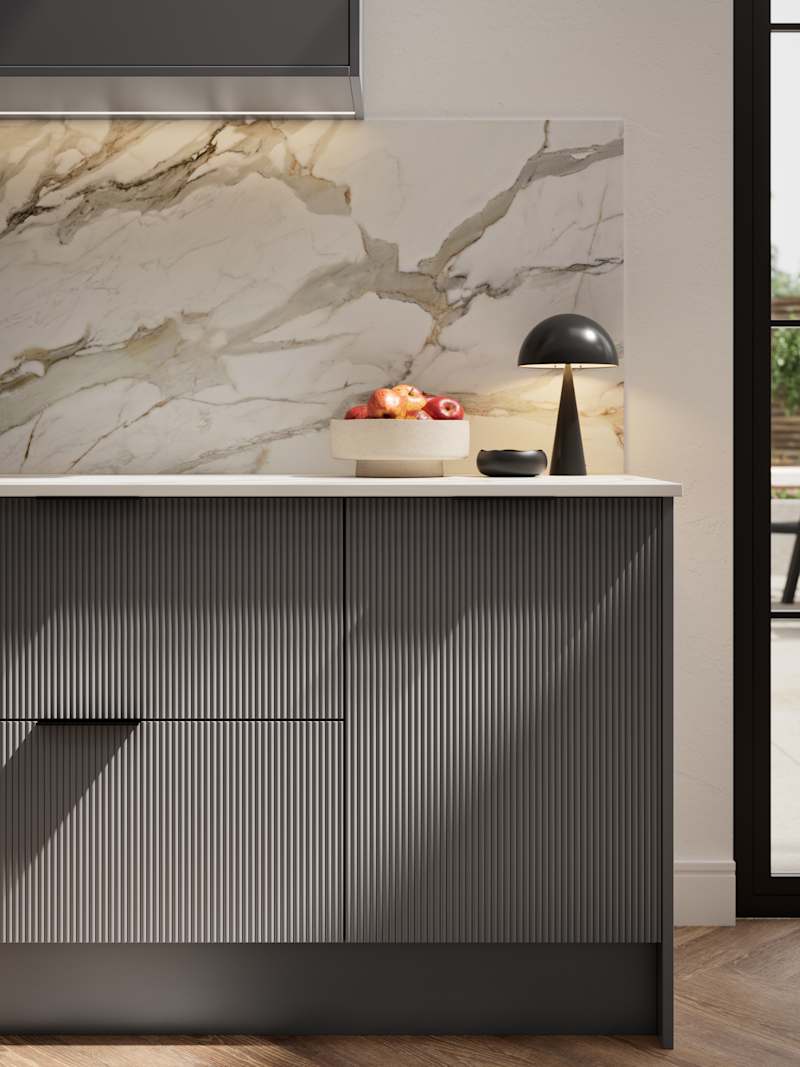 Fluted front kitchen Reed from Magnet in dark grey shade Charcoals, with a marbled splashback and black handles, herringbone wood flooring.