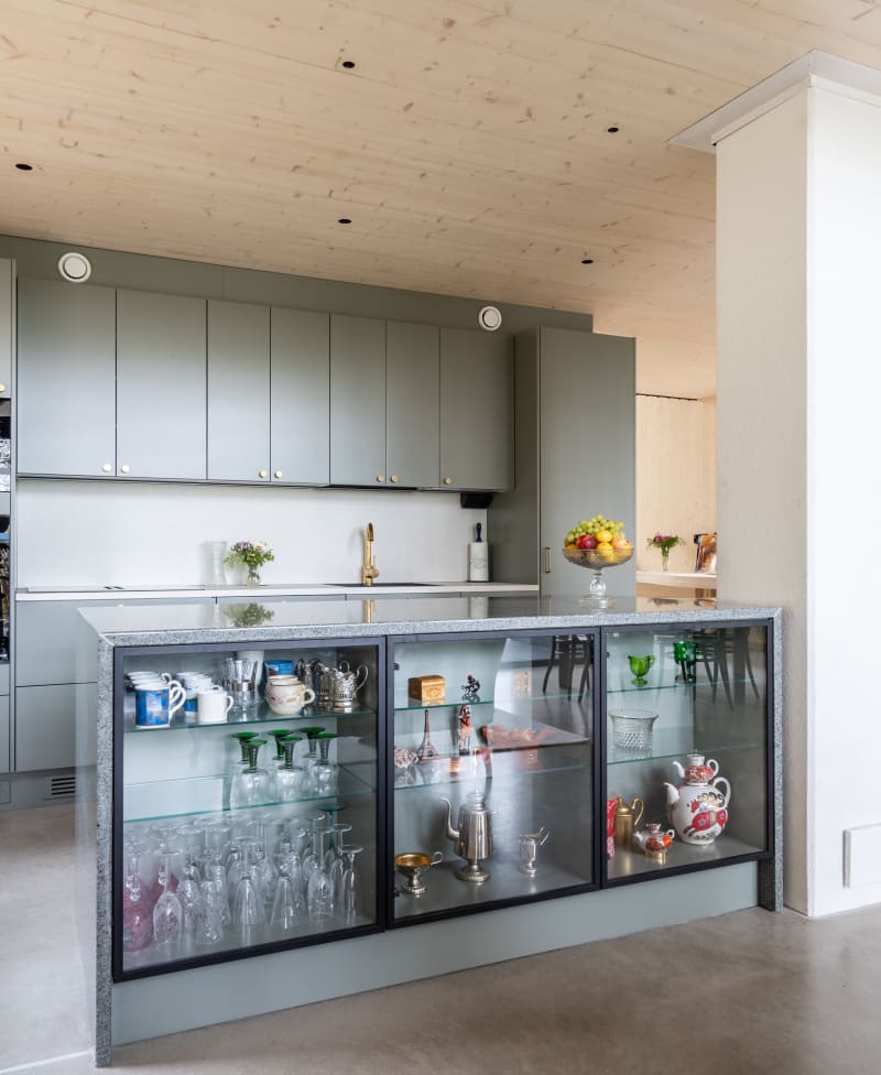 Vihreä keittiö Novartin luonnonvärisessä Havu-sävyssä, messinkinuppeilla, graniittitasoilla ja lasiovilla, joissa on alumiinikehykset keittiön altaassa.