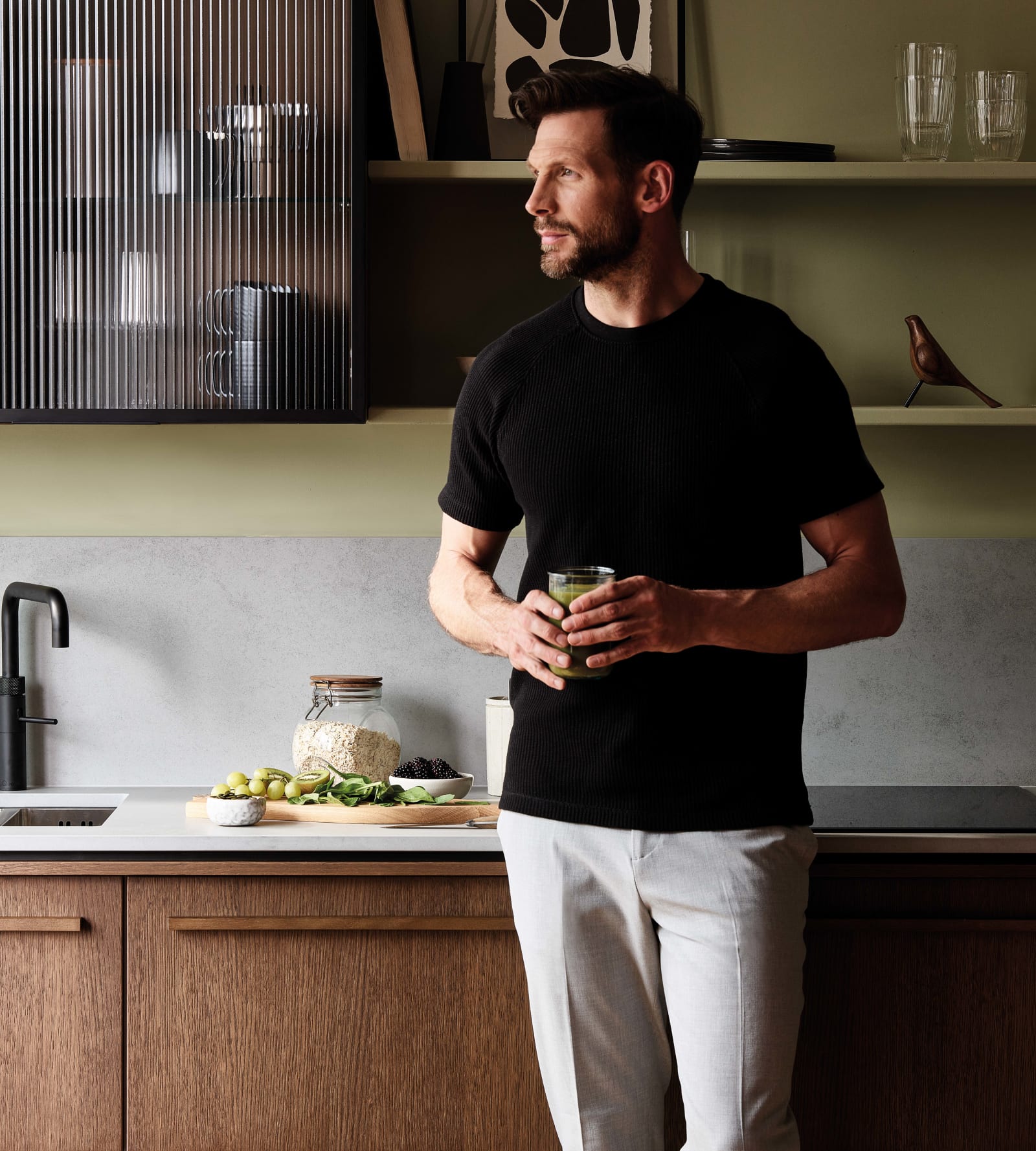 Man holding a glass of green juice leaning towards the cabinet in a Nordic Nature range kitchen