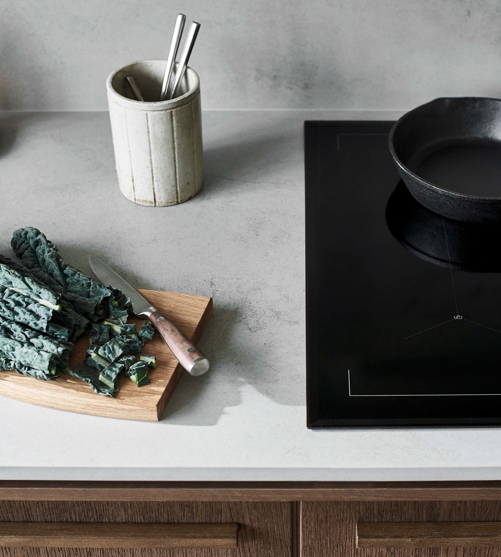 Integrated induction hub from AEG in a Nordic Nature kitchen from Magnet, with a wooden cutting board and handmaid ceramics on the worktop next to it.