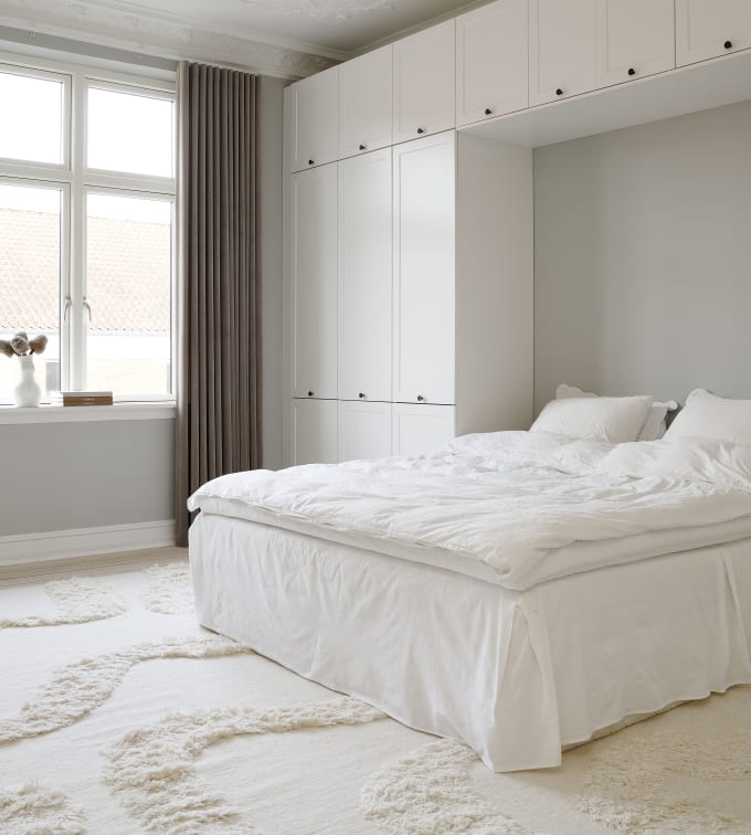 Hvid tidløs garderobe Square Sand fra INVITA omkring en seng med en kommode over, sorte greb på karmdøren