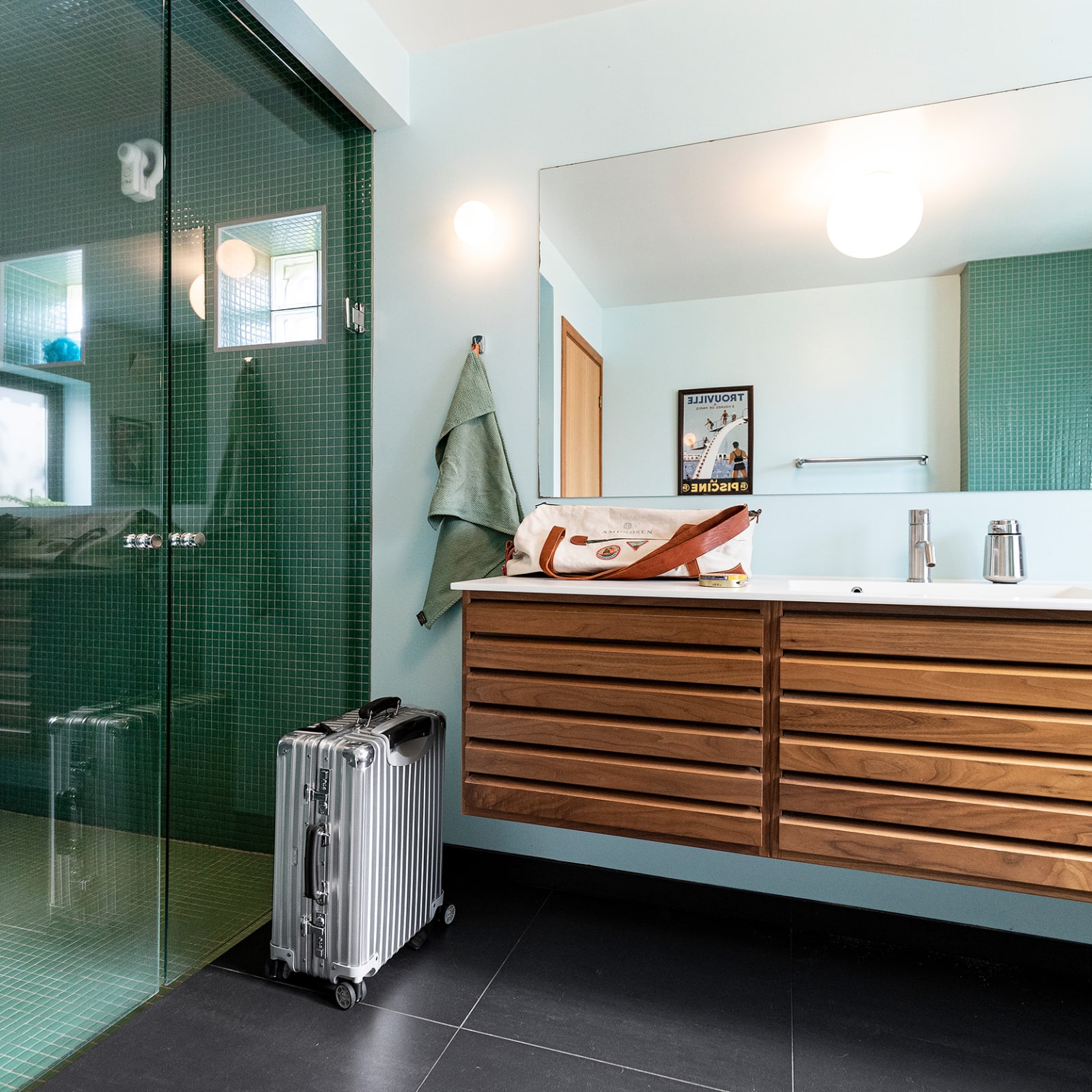 The bathroom is furnished with uno form's original Classic design in walnut and emerald-green mosaic tiles that match the Trouville vintage poster