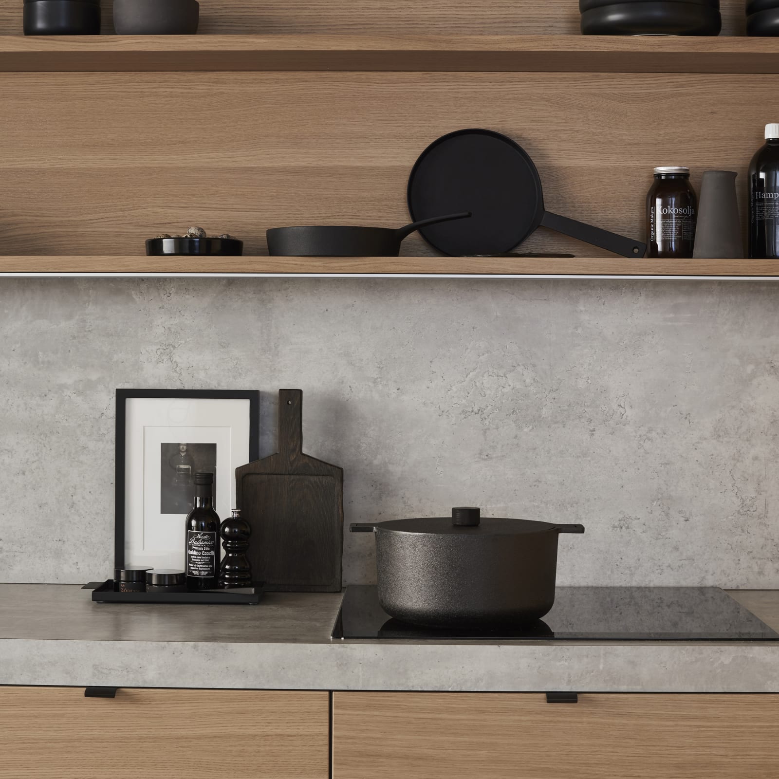 Nærbillede av finér eg natur køkken Athena fra INVITA, med matchende væghylder, laminat bordplade og splashback med betonmotiv, sort håndtag.