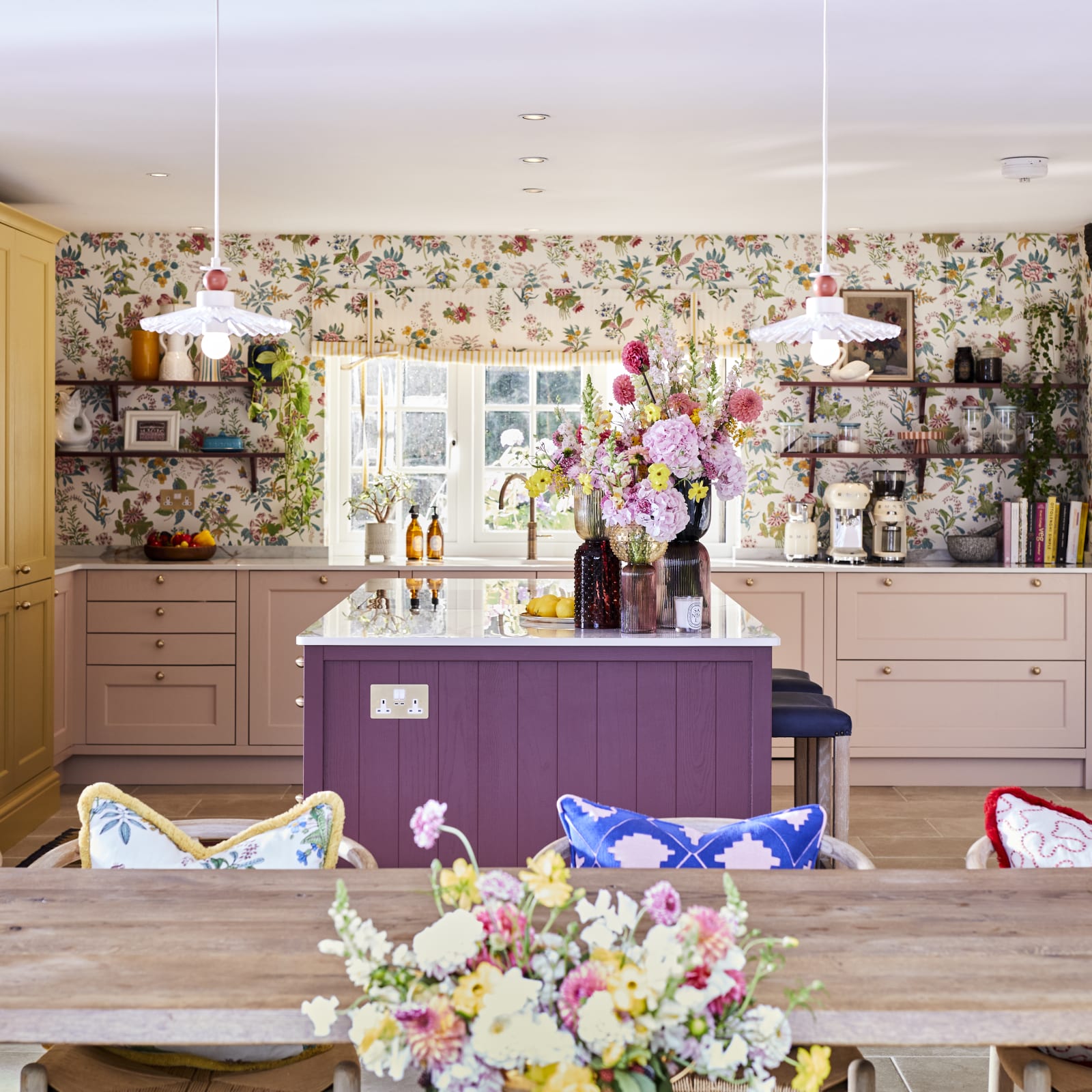 View over wooden table in foreground and Magnet Ludlow kitchen in background, in Sophie Robinson's vibrant maximalist kitchen.