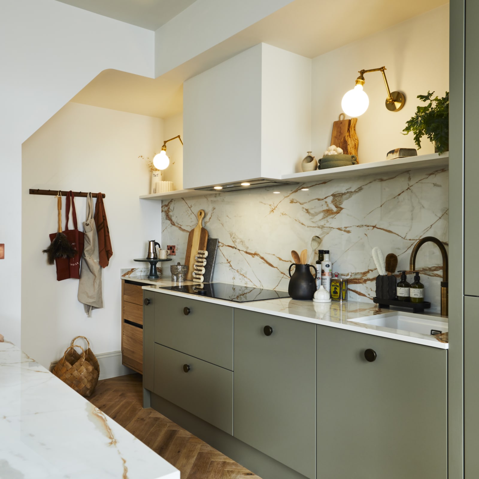 Modern slab Soho Balmoral cabinet paired with modern appliances, a marbled worktop and backsplash, brass details and plants.