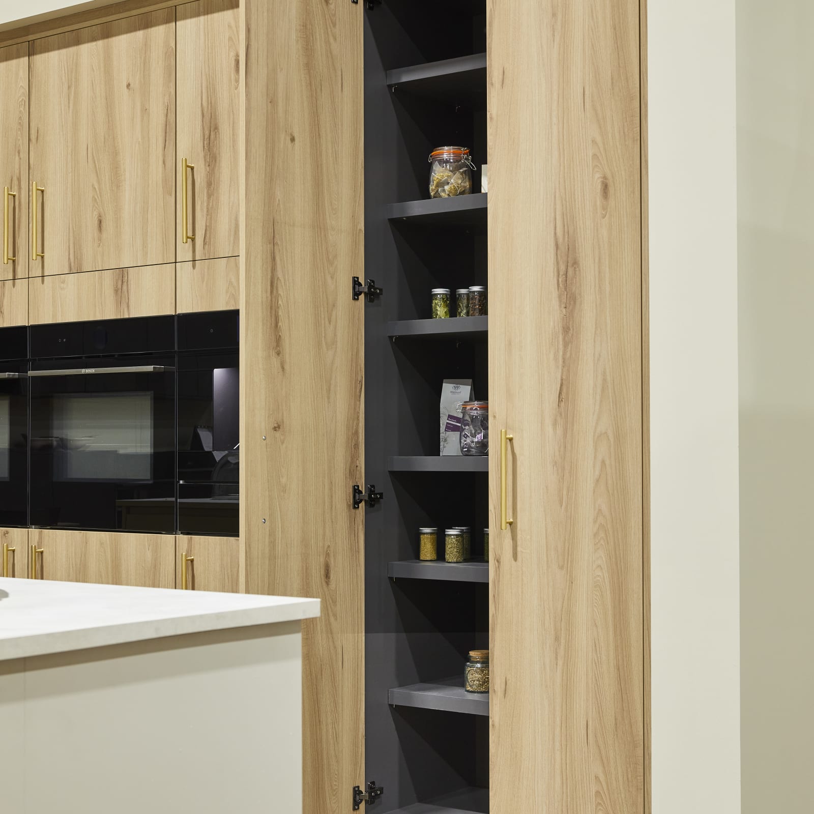 Magnet's modern Portobello kitchen in a light woodgrain décor, larders finished with brass bar handles.