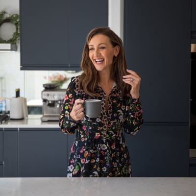 Cath Tyldesley laughing and holding a cup in her chic and contemporary handleless Luna Midnight kitchen from Magnet.