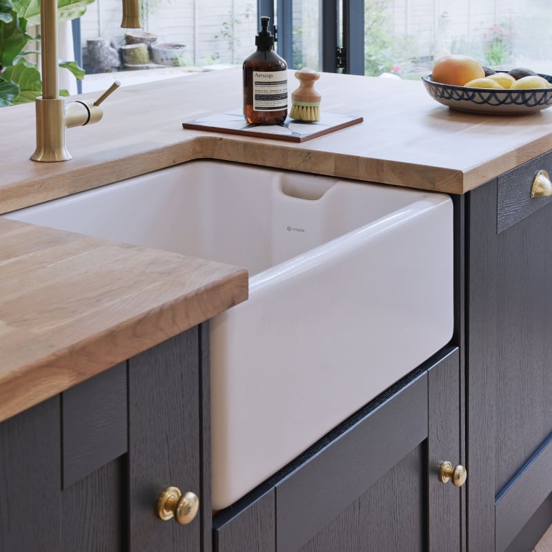 Close-up of Caple Belfast Ceramic sink which adds a rustic charm to the kitchen island. Paired with a wood worktop and brass tap.