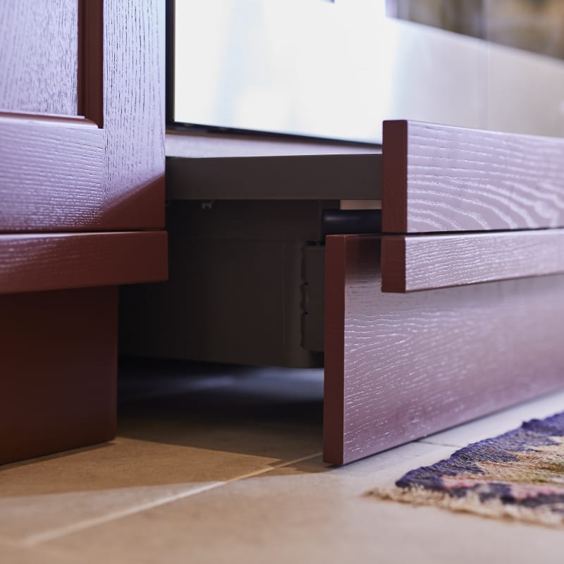 Close-up of pulled out drawers under oven in kitchen island, with traditional Shaker style fronts Ludlow Burlington red, with a tactile woodgrain.