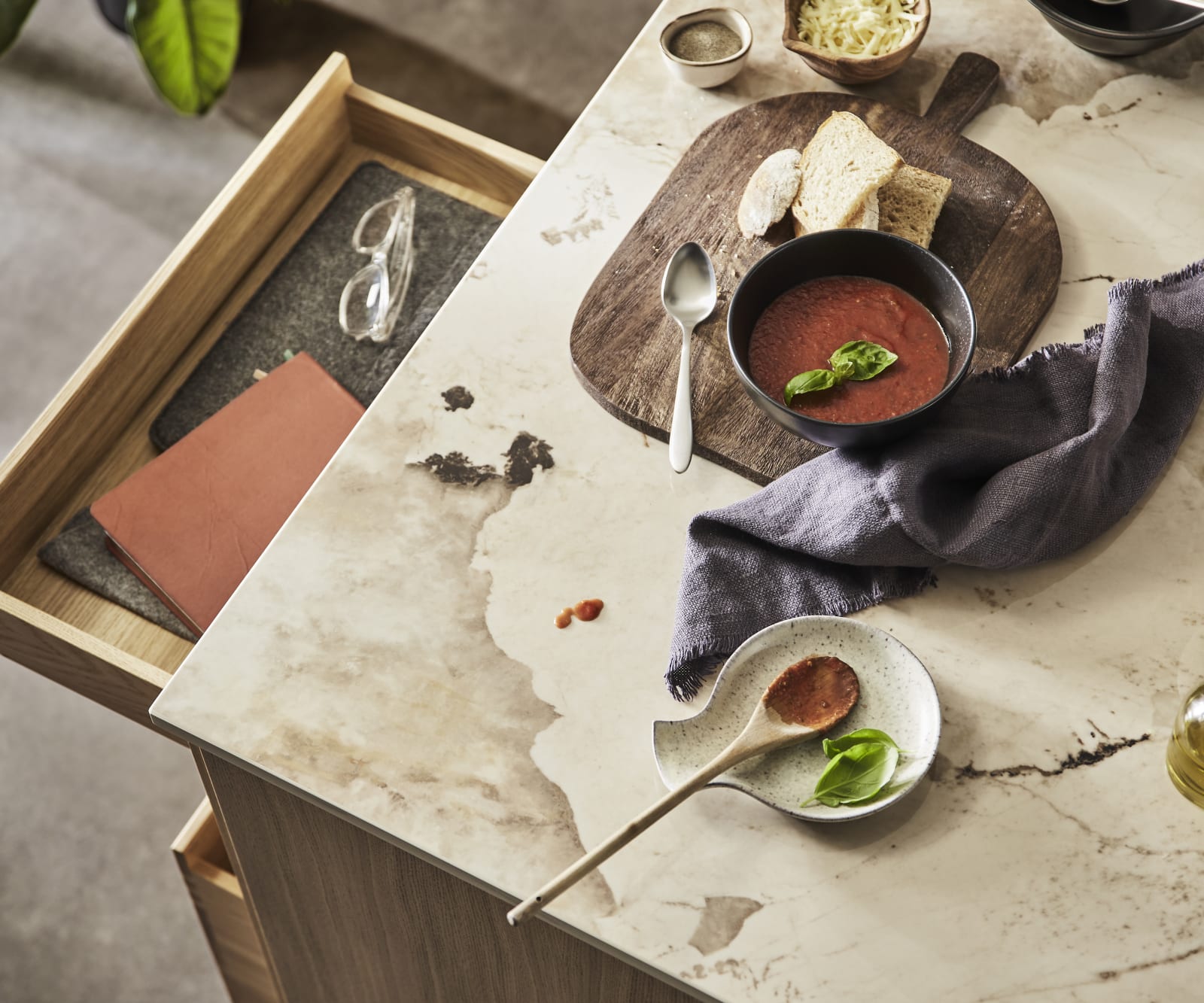 Bird view of kitchen island with Dekton Khalo Worktop, ceramic bowls containing tomato soup, bread and olive oil while an oak drawer is opened.