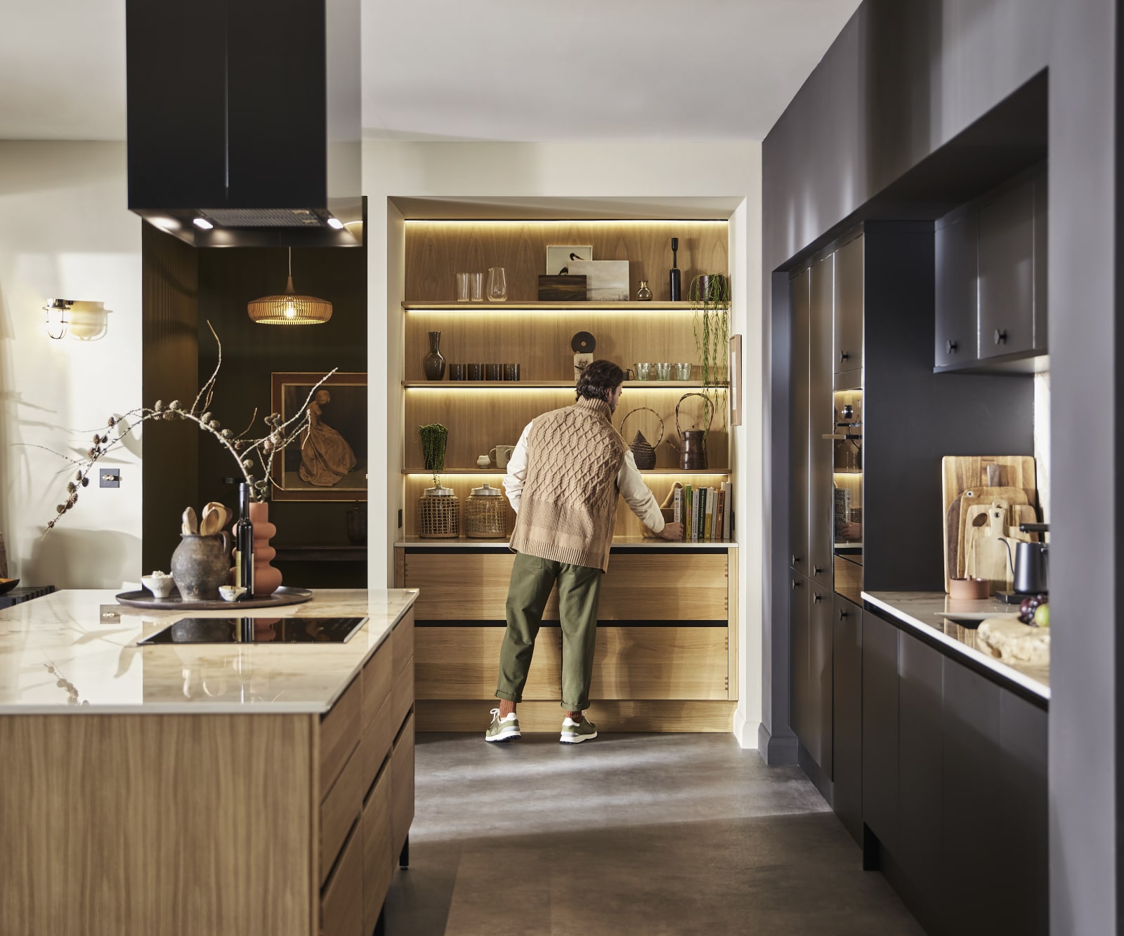 Man organising reaching for cook book in natural oak open shelves with matching wall paneling over Nordic Craft cabinetry.