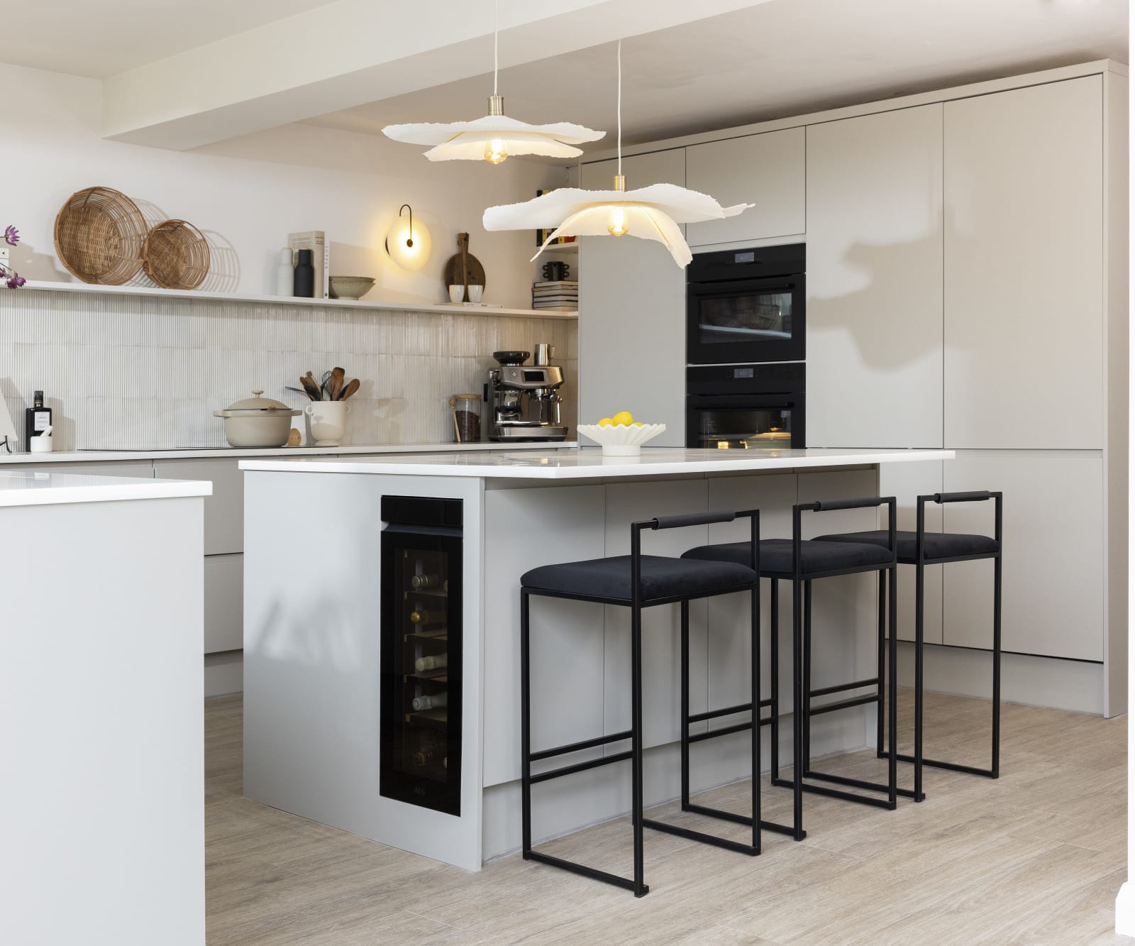 Diagnonal view of kitchen island corner in Yasmin Wyatt's open, light and airy neutral shade handleless Luna kitchen from Magnet with a white Corian worktop in Onyx, two AEG ovens integrated into tall cabinet and a wine cooler integrated into kitchen island.
