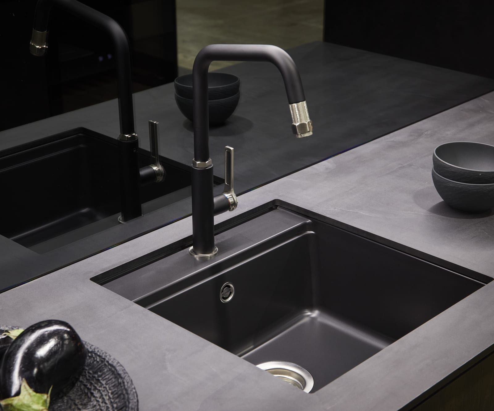 A contemporary kitchen with a matt black sink and tap, dark worktops and modern black glass splashback.