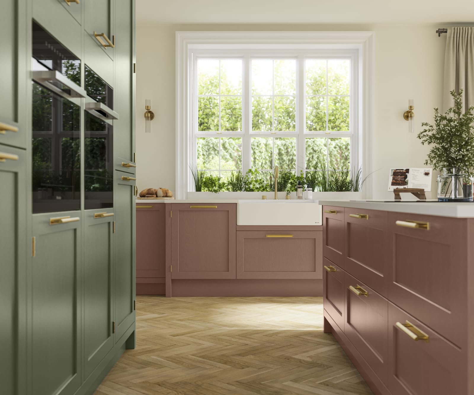 Tall cabinetry with built-in ovens and kitchen island with white worktop in Wardley kitchen from Magnet in shades Clay and Thyme, matched with brass handles and a vase of flowers on the countertop.