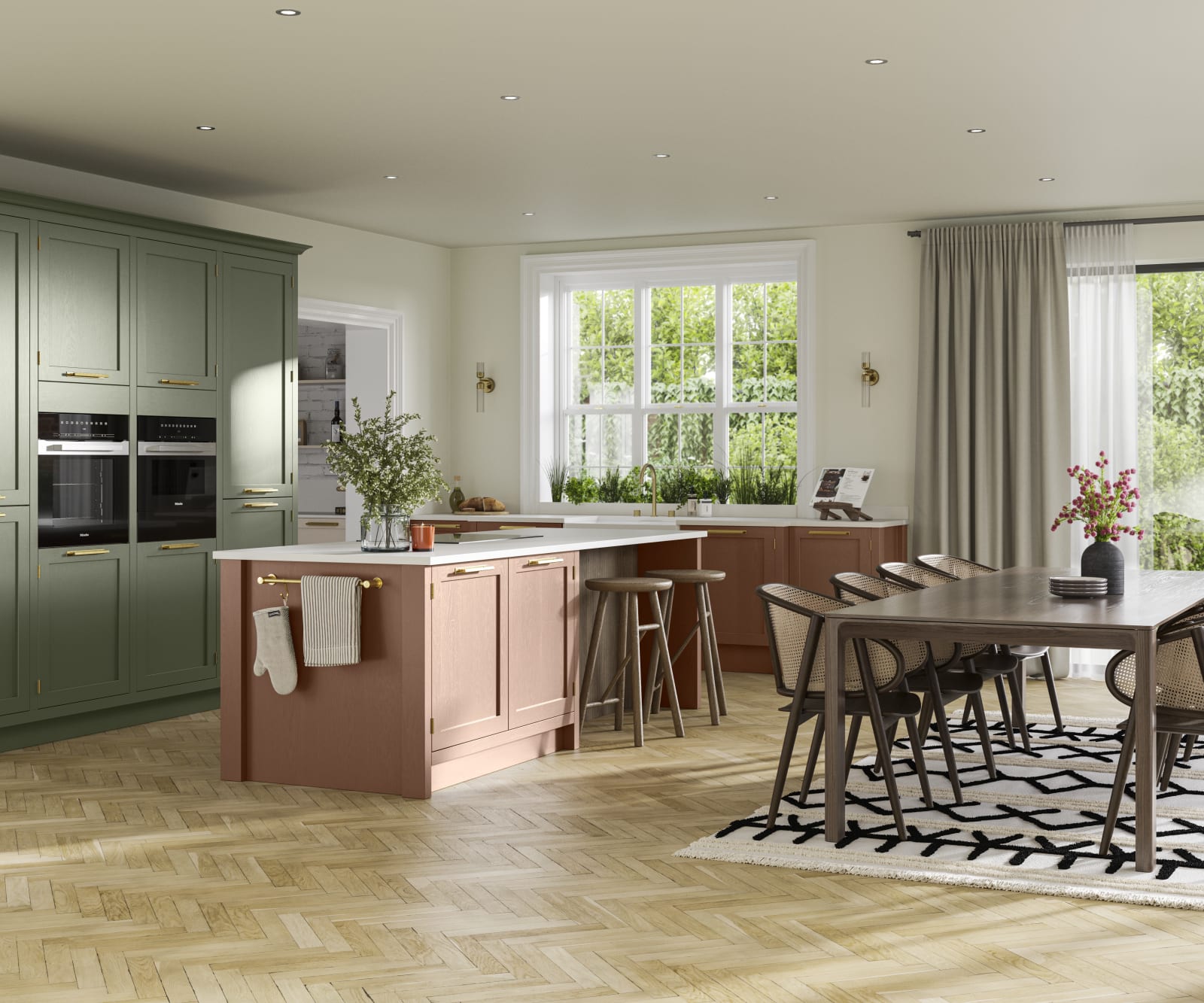 Open floorplan kitchen and dining rool with tall Wardley kitchen cabinetry from Magnet with built-in ovens and a kitchen island, in the shades Thyme and Clay, with a large wooden dining room table.