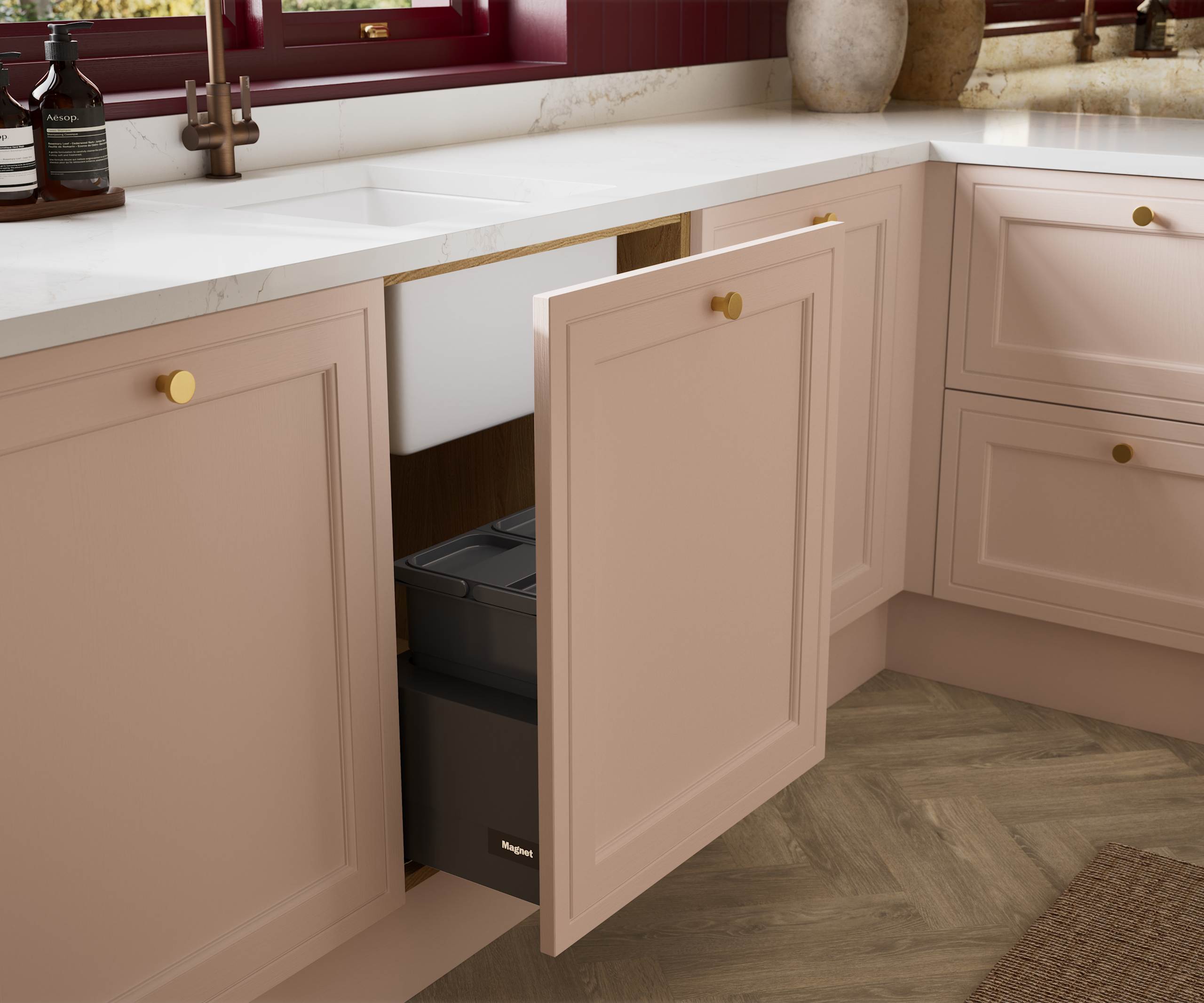 Opened sink drawer in painted wood grain Shaker style Bewdley kitchen with cabinets in light pink shade Chalk Blush, marbled worktop and brass knobs.