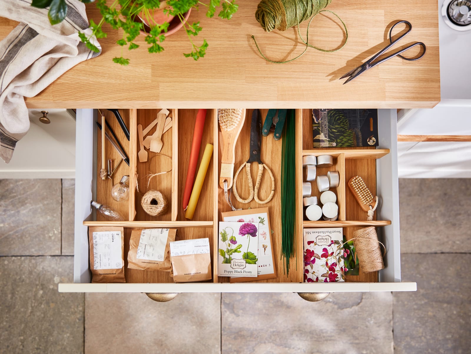 Overhead view of opened drawer in Winchester Sage utility room, with oak inserts sorting paper bags of seeds and other gardening tools.