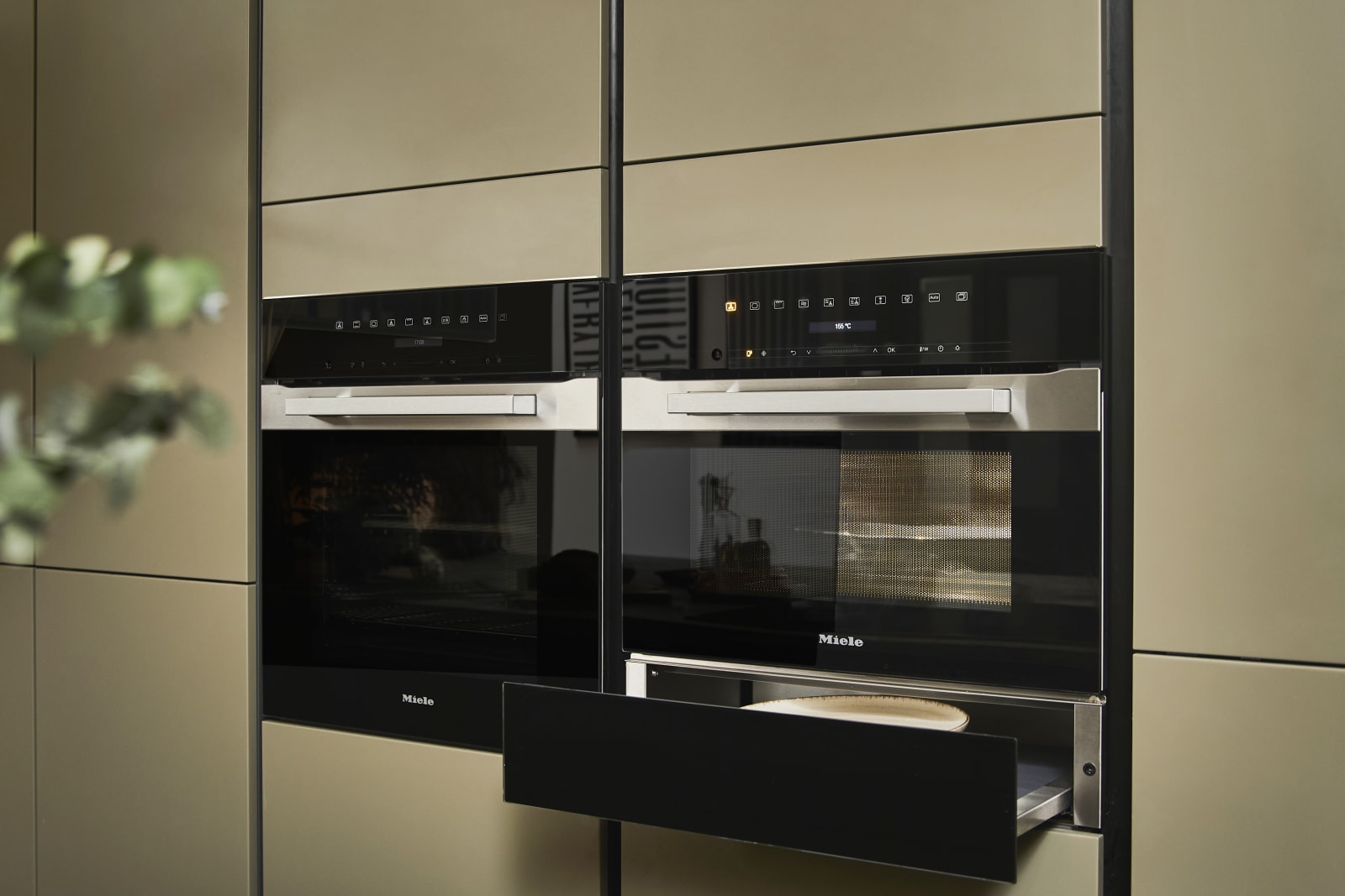 Built-in Ovens with opened warming drawer in modern slab front Balmoral Soho cabinetry from Magnet, Dekton in Ceppo worktop of kitchen island in foreground.