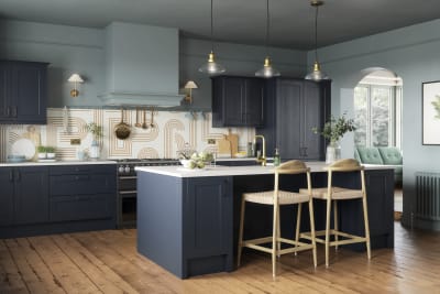 Modern country-style Ludlow kitchen in dark blue shade Midnight, with lighter blue walls, wooden floors and wooden barstools by kitchen island.