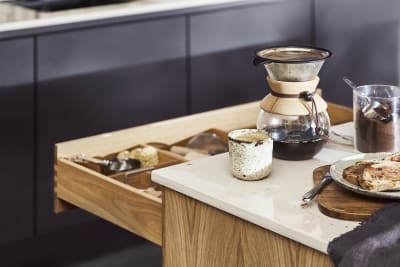 Close-up of opened oak drawer in Nordic Craft kitchen island, with breakfast served on handmade ceramics on the worktop.