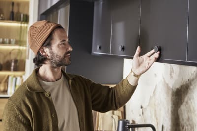 Man wearing clothes in earth tones opening a top cabinet in Hoxton Sumi Black