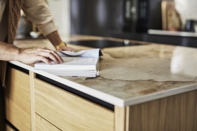 Close-up of Nordic craft kitchen island, with a beautiful marbled worktop as someone is checking a recipe in a cook book.