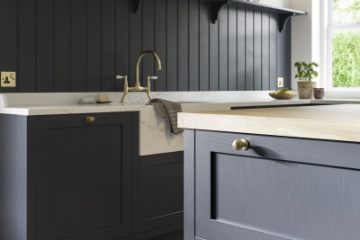 Closeup of dark blue Shaker kitchen Wardley, with painted timber finish and narrow framing. Paired with a brass kitchen tap and blue matching wall panelling.