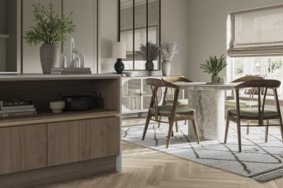 Integra Ascoli kitchen, close-up view of kitchen island with dining table in background. Light and earthy toned interior with plants.