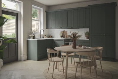 The Ambleside Shaker kitchen in a dark green, seen with a wooden dining table.