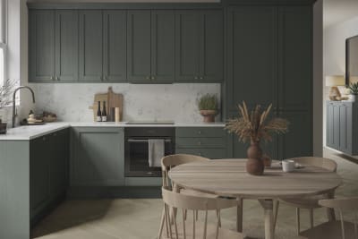 A Shaker kitchen with dark green cabinets and a wooden table.